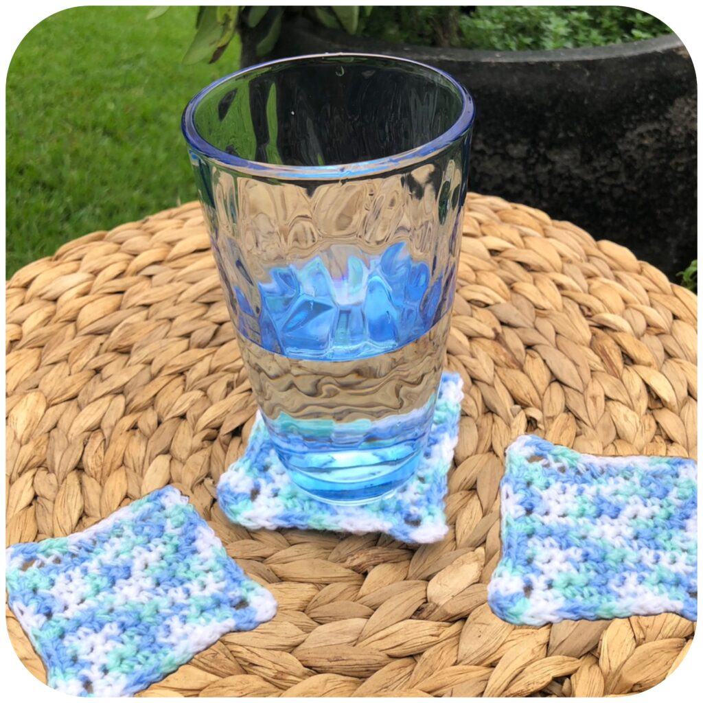Glass of water on a crocheted coaster with another coaster either side. These are on a woven grass mat